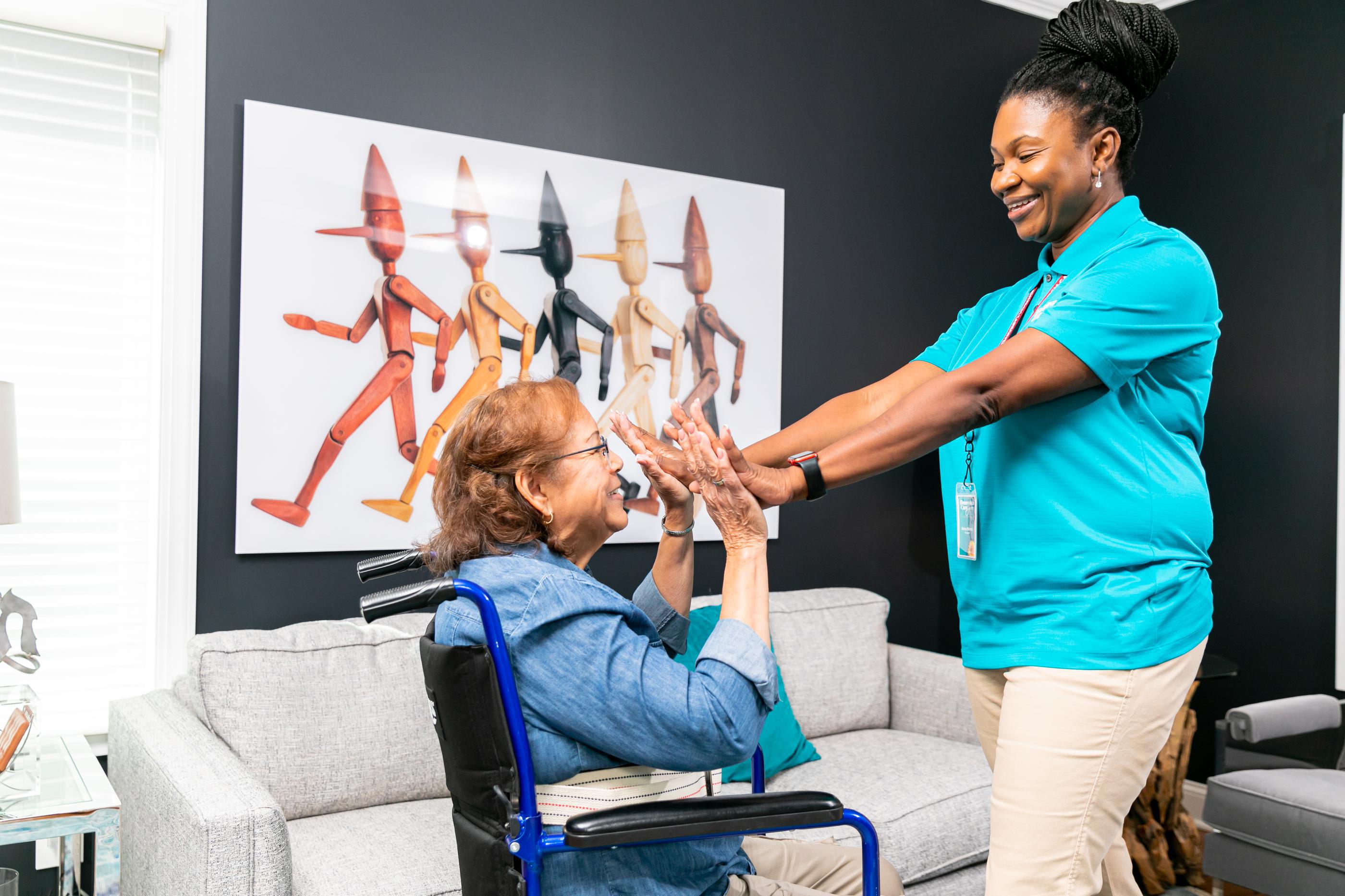 female caregiver giving double high fives to senior woman in wheelchair