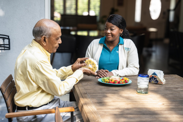 man taking daily pills with food while nurse sits at table with him