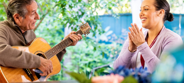 man playing guitar while woman smiles and claps