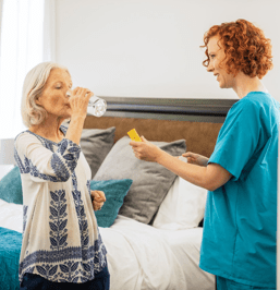 woman helping elderly woman take medication 