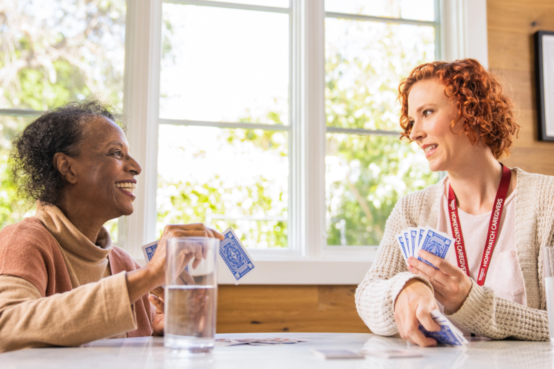 an elderly woman playing cards with a caregiver